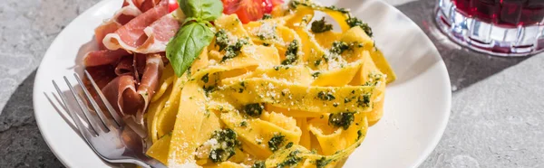 Domatesli lezzetli Pappardelle, pesto ve çatallı prosciutto gri yüzeyde kırmızı şarap, panoramik çekim