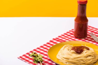 Sarı arka planda beyaz yüzeyde kişniş yanında domates soslu spagetti.