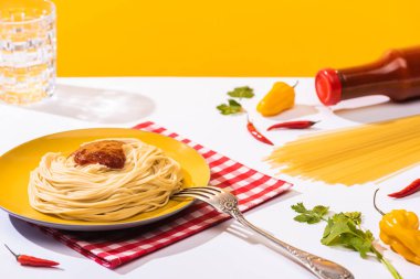Biberin yanında ketçaplı lezzetli spagetti ve sarı arka planda beyaz yüzeyde bir bardak su.