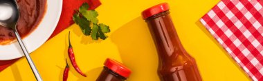 Tabakta domates sosu ve kırmızı biberli şişeler ve sarı arka planda yeşillik, panoramik çekim