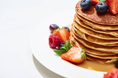 close up view of delicious pancakes with honey, blueberries and strawberries on plate on white surface clipart