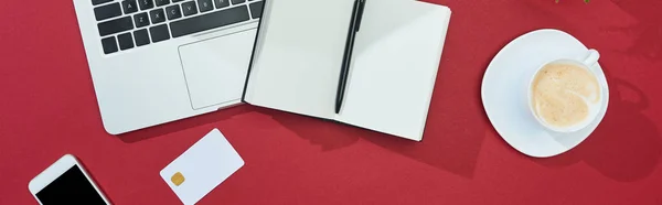 带智能手机 笔记本电脑 带钢笔的笔记本 全景照片的红色背景信用卡顶部视图 — 图库照片