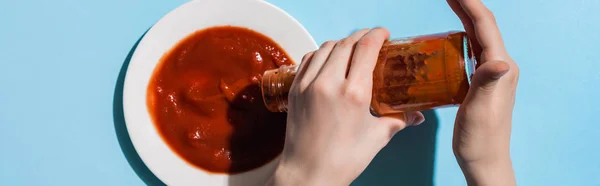 女人把美味的番茄酱从瓶子里倒到盘子里 倒入蓝色的表面 全景拍摄 — 图库照片