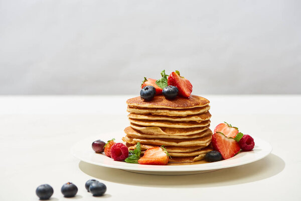 вкусные блины с черникой и клубникой на тарелке на белой поверхности, изолированные на серой
