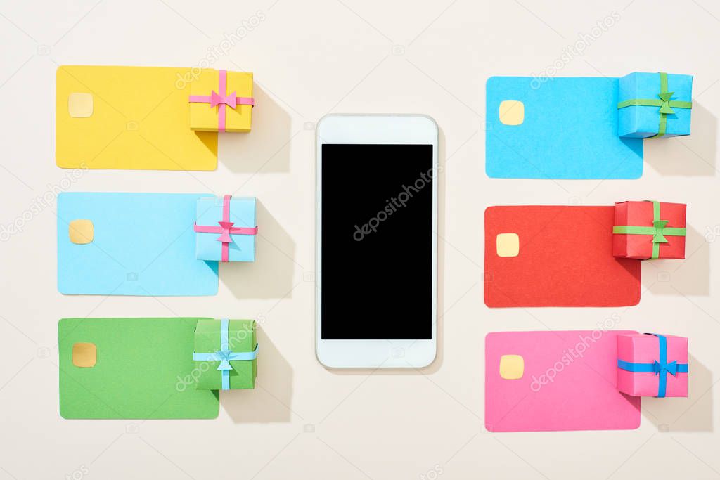 top view of multicolored empty credit cards, smartphone and gift boxes on white background