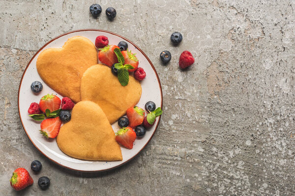 top view of heart shaped pancakes with berries on grey concrete surface