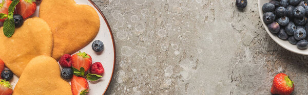 top view of heart shaped pancakes with berries on grey concrete surface, panoramic shot