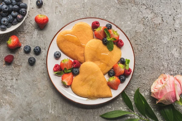 Ovanifrån Hjärtformade Pannkakor Med Bär Grå Betong Yta Nära Ros — Stockfoto