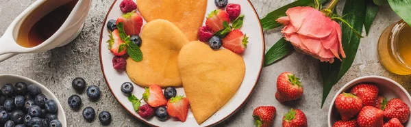 Gri beton yüzey üzerinde böğürtlenli, kalp şeklindeki gözlemeler çiçek açan gül, bal ve akçaağaç şurubu, panoramik çekim