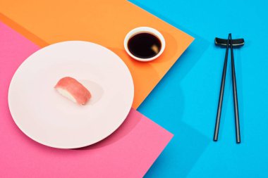 Soya sosu yanında ton balıklı taze nigiri ve pembe, mavi, turuncu yüzey üzerinde çubuklar.