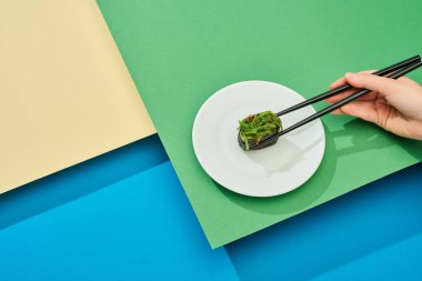 Taze nigiri yiyen bir kadının kırpılmış görüntüsü. Çok renkli yüzey üzerinde çubukları olan deniz yosunuyla.