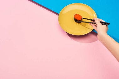 Mavi, pembe yüzey üzerinde yemek çubukları olan kırmızı havyarlı taze nigiri yiyen kadın görüntüsü.