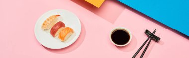 Soya sosu yanında somon, ton balığı ve karides ile taze nigiri ve mavi, pembe, turuncu yüzey üzerinde çubuklar, panoramik çekim