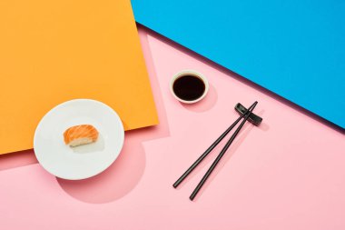 Soya sosu yanında somon somonu ve mavi, pembe, turuncu yüzey üzerinde çubuk taze nigiri