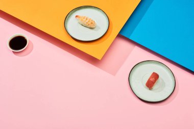 Mavi, pembe, turuncu yüzeyde soya sosu yanında ton balığı ve karides ile taze nigiri.