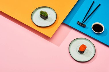 Soya sosunun yanında deniz yosunu ve kırmızı havyar ile taze nigiri ve mavi, pembe, turuncu yüzey üzerinde çubuklar.