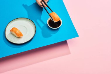 Mavi ve pembe arka planda soya sosuna taze nigiri somonla soya sosu katan kadın görüntüsü.
