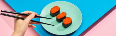 Mavi arka planda kırmızı havyarlı taze nigiri yiyen kadın manzarası, panoramik çekim.