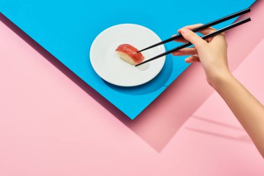 Mavi ve pembe arka planda ton balıklı taze nigiri yiyen bir kadın görüntüsü.