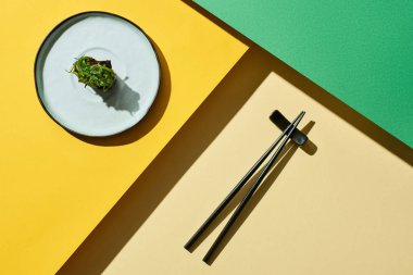 Yeşil ve sarı yüzey üzerinde yemek çubuklarının yanında deniz yosunlarıyla taze nigiri manzarası