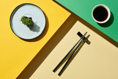 Soya sosu yanında deniz yosunuyla taze nigiri ve yeşil ve sarı yüzey üzerinde çubuklar.