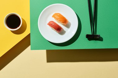 Soya sosu yanında somon ve ton balıklı taze nigiri ve yeşil ve sarı yüzeyde çubuklar.