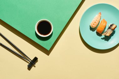 Soya sosunun yanında somon, karides ve yılan balığı ve yeşil ve sarı yüzey üzerinde çubuklar bulunan taze nigiri manzarası.