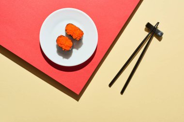 Kırmızı ve bej yüzey üzerinde yemek çubuklarının yanında kırmızı havyar bulunan taze Nigiri 'nin üst görüntüsü