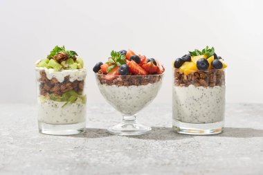 Gri beton yüzeyde meyveler ve böğürtlenlerle beyazı izole edilmiş bardaklarda lezzetli granola.
