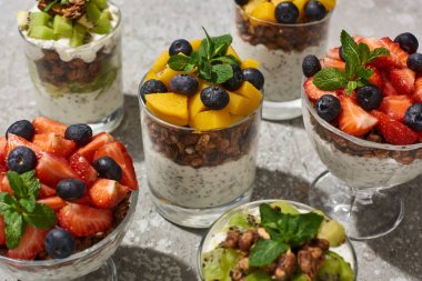 Gri beton yüzeyinde meyve ve böğürtlen dolu bardaklarda lezzetli granola.