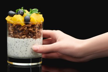 Kırpılmış bir kadın elinde bardakla taze granola konserve şeftali, yabanmersini ve chia tohumlarıyla siyah üzerine izole edilmiş