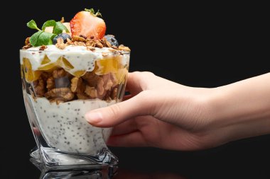 Kırpılmış bir kadın elinde bardakla taze granola konserve şeftali, böğürtlen, ceviz ve chia tohumlarıyla siyah üzerine izole edilmiş