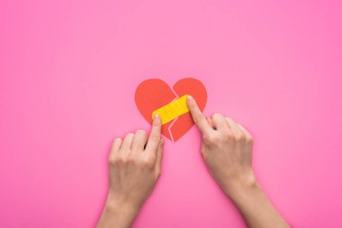 Kırık kalbe yama yapan, pembe arka planda izole edilmiş kadın görüntüsü.