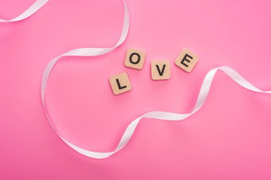 Kıvrımlı kurdele ve ahşap blokların üst görüntüsü pembe harflerle izole edilmiş.