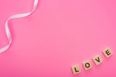 Kurdelenin üst görüntüsü ve pembe üzerine izole edilmiş tahta küplere yazılmış harfler.