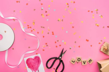 top view of valentines confetti, empty compact disk, scissors, gift boxes, greeting card and love lettering on wooden cubes on pink background clipart