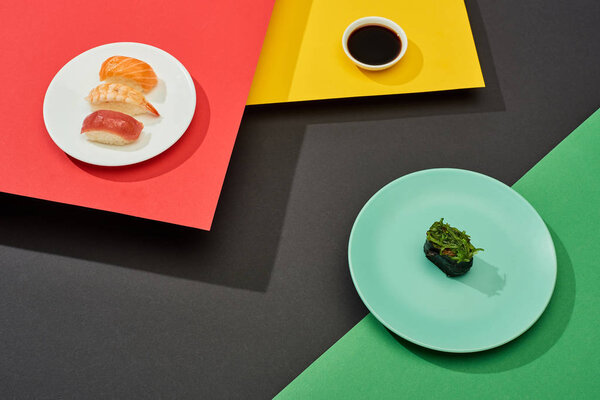 fresh nigiri with salmon, shrimp and tuna near soy sauce and nigiri with seaweed on red, yellow, green and black surface