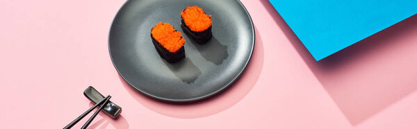 fresh nigiri with red caviar near chopsticks on blue, pink background, panoramic shot