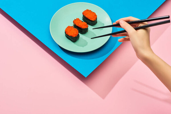 cropped view of woman eating fresh nigiri with red caviar on blue, pink background