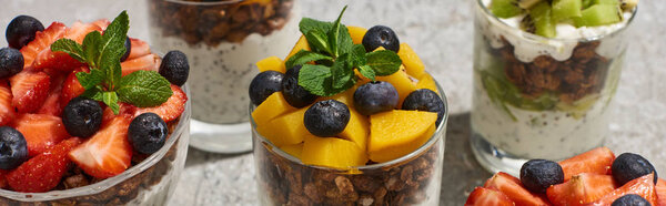 delicious granola in glasses with fruits and berries on grey concrete surface, panoramic shot