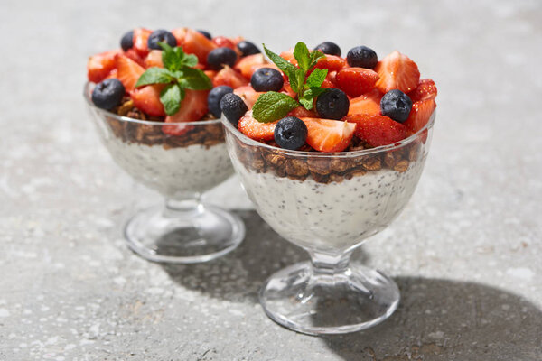selective focus of delicious granola with berries and yogurt with chia seeds on grey concrete surface
