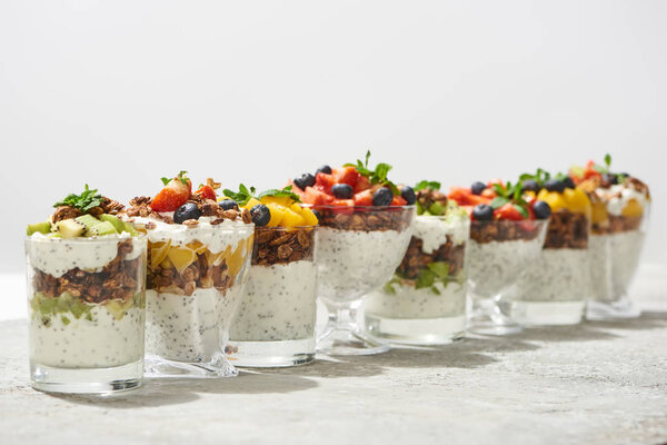 селективный фокус вкусной гранолы в стаканах с фруктами и ягодами на серой бетонной поверхности, изолированной на белом
