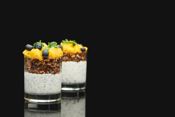 selective focus of fresh granola with canned peach, blueberries and chia seeds isolated on black