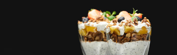 selective focus of fresh granola with canned peach, berries, walnuts and chia seeds isolated on black, panoramic shot