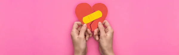 cropped view of holding broken paper heart with patch isolated on pink background, panoramic shot