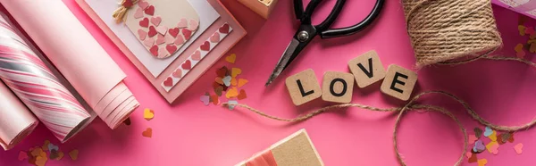 バレンタインデコレーション はさみ 包装紙 ツイン ギフト グリーティングカードとピンクの背景に木製のキューブ上の愛のレタリング パノラマショットのトップビュー — ストック写真