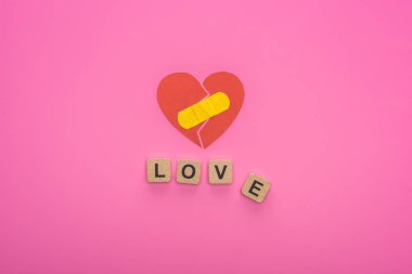 Kırık kalbe yakın tahta küplerde pembe arka planda yamayla yazılmış aşk mektuplarının üst görüntüsü.