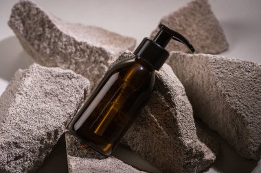 Gri arkaplanda kayaların üzerinde kozmetik şişe.