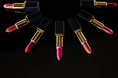 Lüks tüplerdeki çeşitli rujlar siyah üzerine izole edilmiş daire şeklinde dizilmiş.