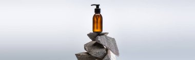 dispenser cosmetic bottle on stones on white background with back light, panoramic shot clipart